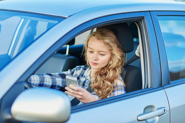 Young woman engaging in distracted driving while using her smartphone and driving a car at the same time.