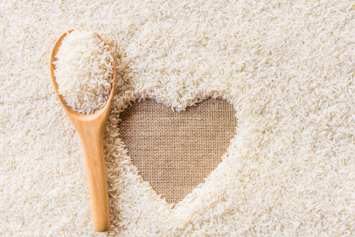 rice in wooden Spoon on rice background Space in the middle of a heart. sackcloth is background