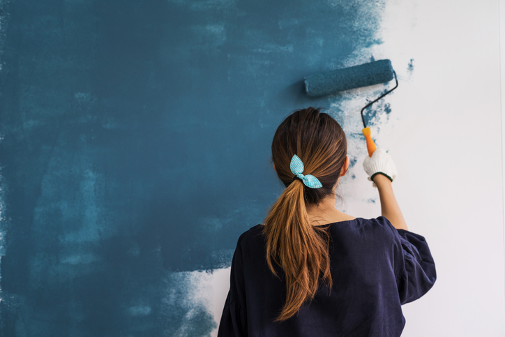 Woman painting a white wall blue with a paint roller for a home improvement project.