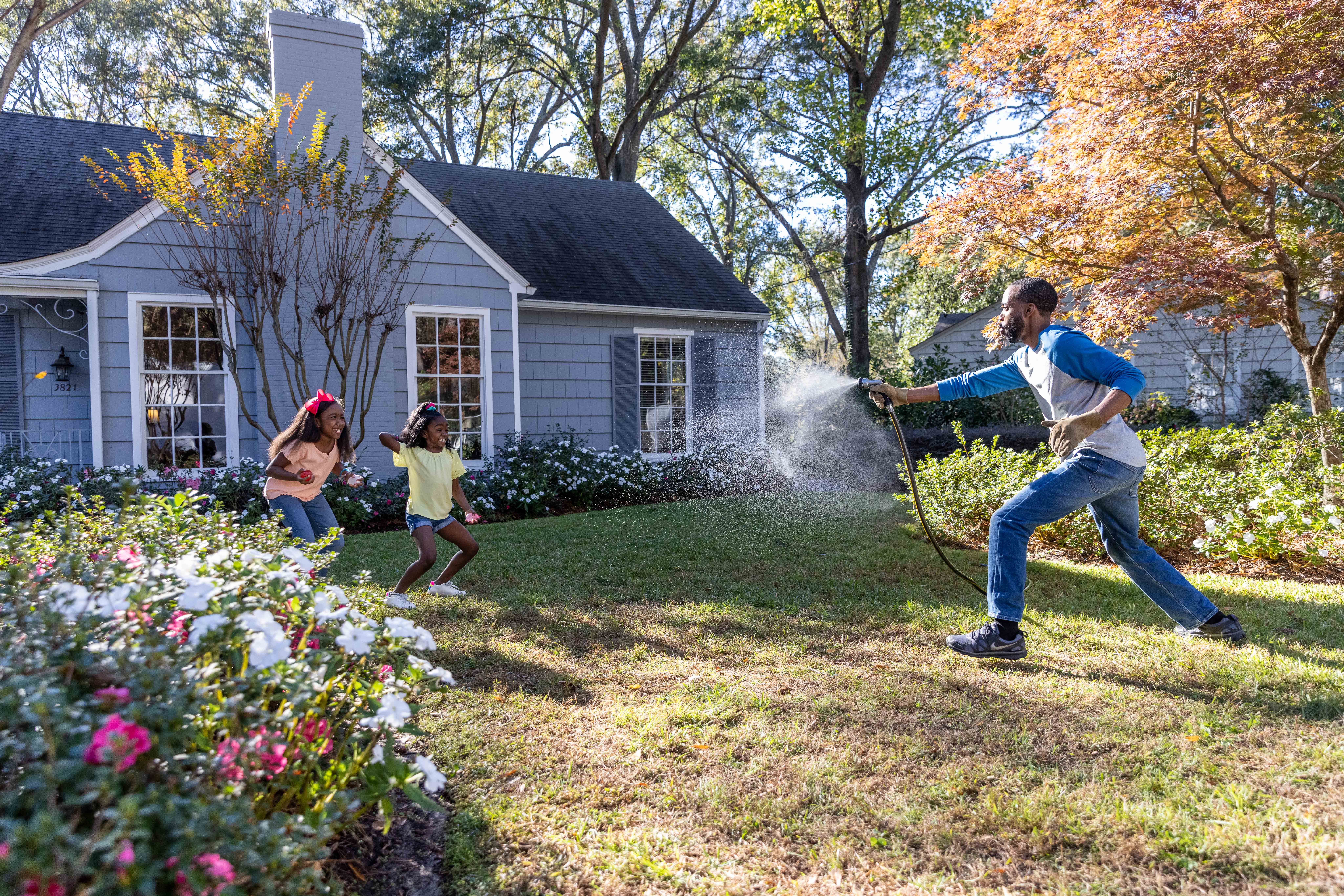 African-American dad and two daughters playing in the front yard of their home.